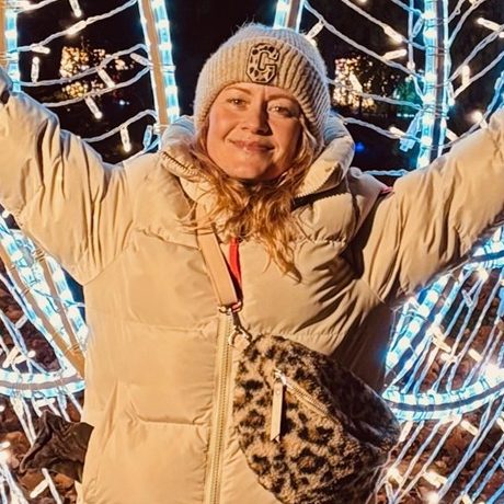 Frau in weißer Jacke mit Mütze und Leopardenhandtasche, umgeben von Lichtern.